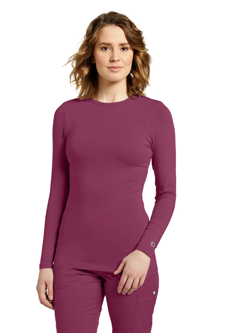 Woman wearing a White Cross 207 long-sleeve underscrub in Raspberry Coulis and pants on a white background