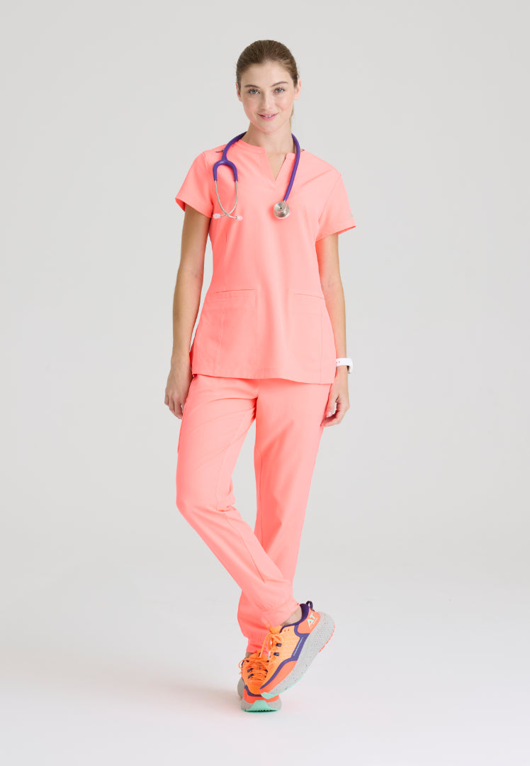Woman wearing a Skechers Coral Fizz medical scrub set (SKT259 scrub shirt and SKP552 jogger scrub pant) with a stethoscope on a light gray background