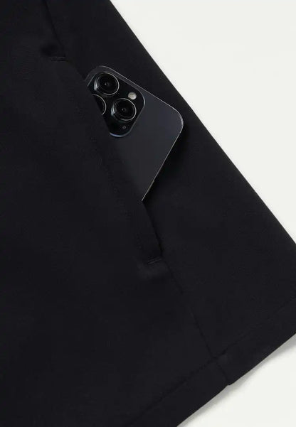 Detailed view of Jaanuu Platt men's scrub shirt in black with a black phone places in the side pocked with a white background