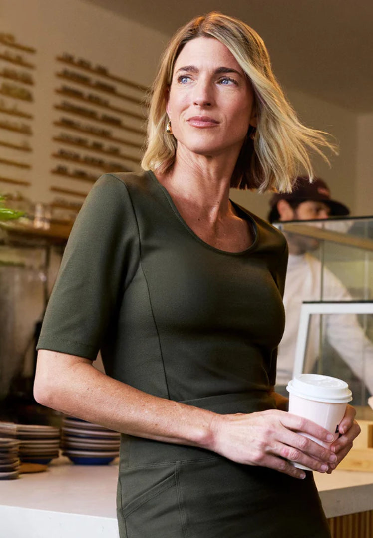 Woman in a green Jaanuu scrub set holding a coffee cup in a cafe setting