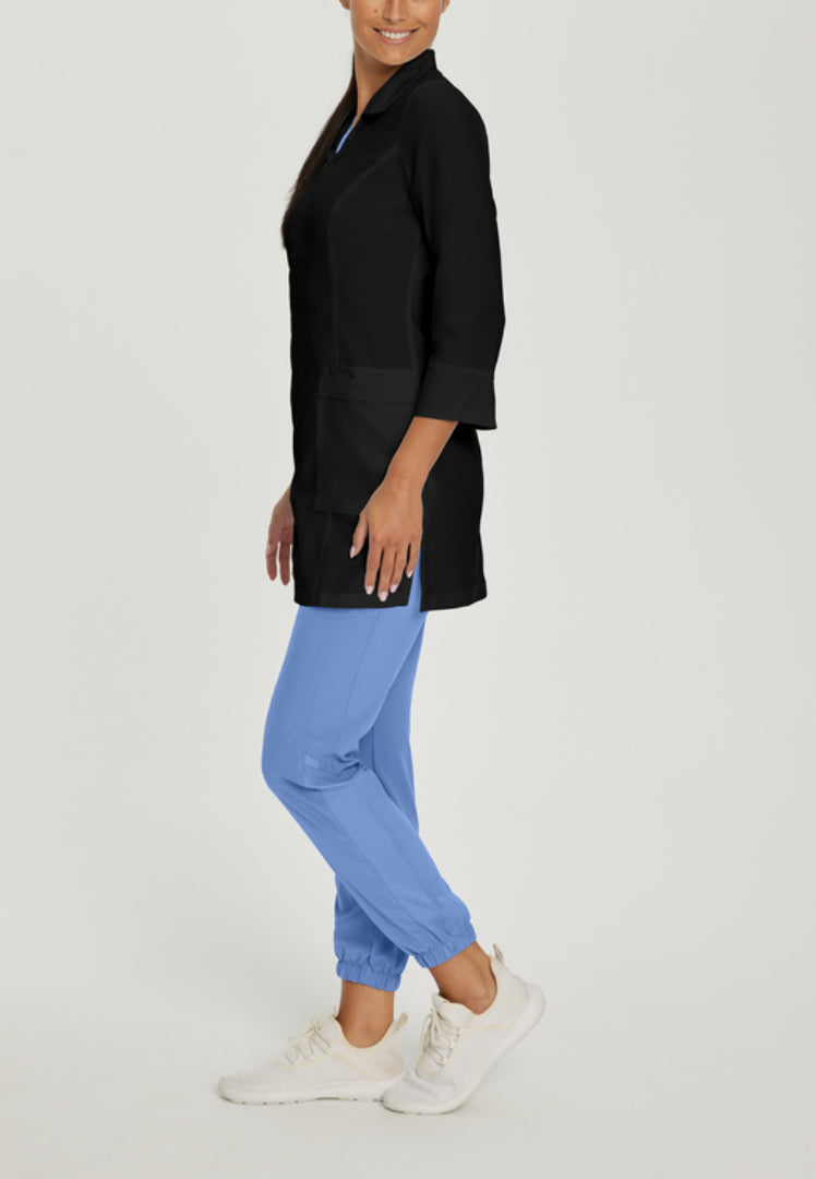 Side view of a person wearing a White Cross 2417 black lab coat and blue pants on a light gray background