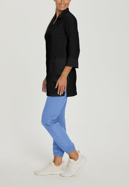 Side view of a person wearing a White Cross 2417 black lab coat and blue pants on a light gray background