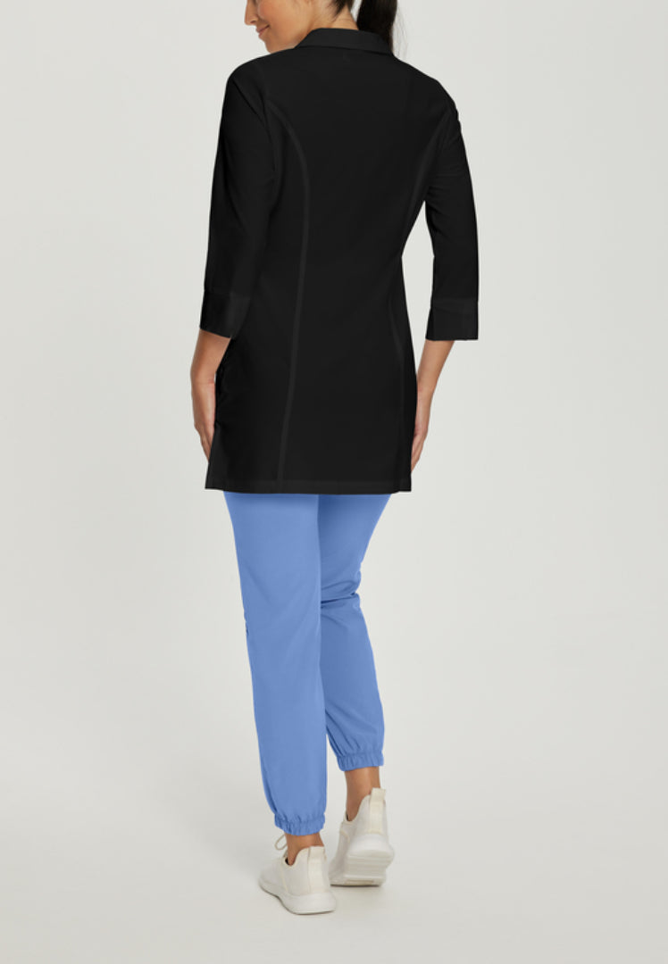 Back view of a person wearing a White Cross 2417 black lab coat, blue pants, and white shoes on a light gray background