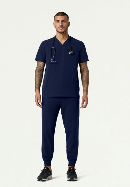 Full body view of a man wearing a navy blue Jaanuu medical scrub set and a stethoscope on a white background