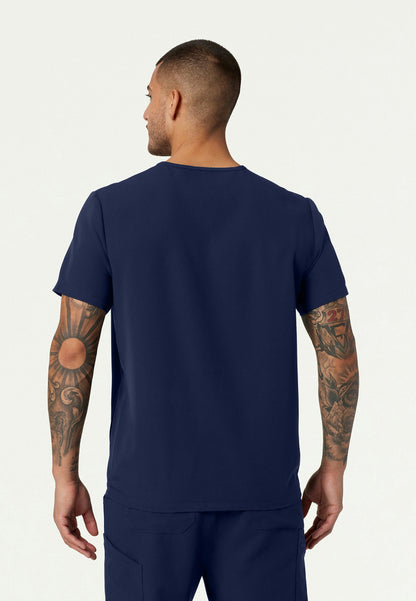 Back view of a man wearing a navy blue  Jaanuu Platt v-neck scrub shirt and pants on a white background