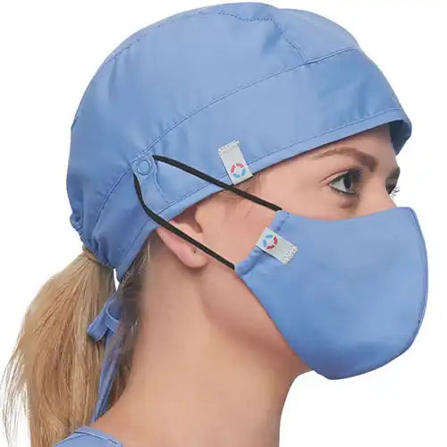 A side profile of a healthcare worker wearing a light blue surgical cap and matching face mask, available at 'The Uniform Store'. The cap is secured with an adjustable tie-back closure, while the mask features comfortable ear loops with a snug fit, both designed for safety and style as part of the store's scrub accessories line.