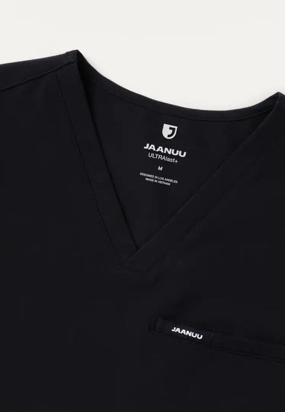Detailed view of a Jaanuu men's Platt V-neck scrub shirt in black with Jaanuu branding on a white background
