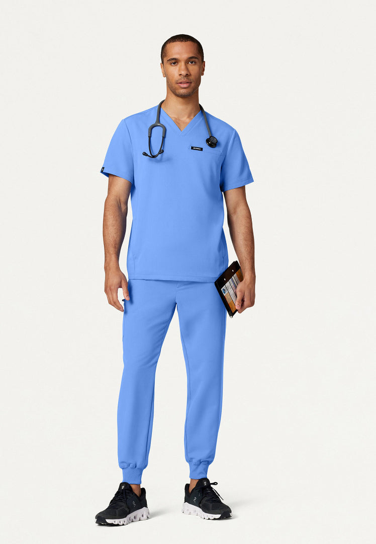 Man wearing a ciel blue Jaanuu scrub set against a white background