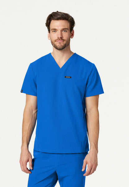 Man wearing a Jaanuu Platt royal blue V-neck scrub top with a visible brand logo on a white background
