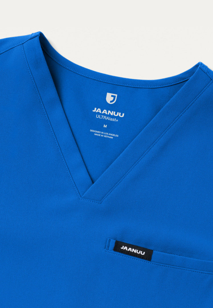 Detailed view of the Jaanuu royal blue scrub top v-neck with 'Jaanuu' pocket branding on a white background