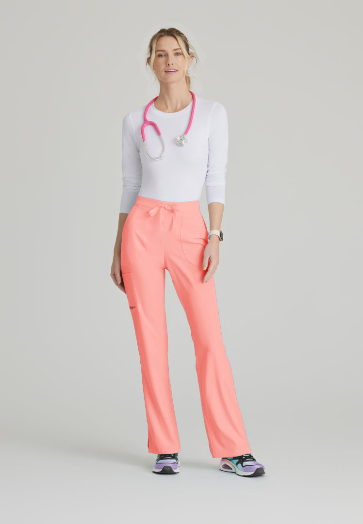 Woman wearing a white underscrub shirt and Skechers SK201 Coral Fizz scrub pants, standing against a light gray background.
