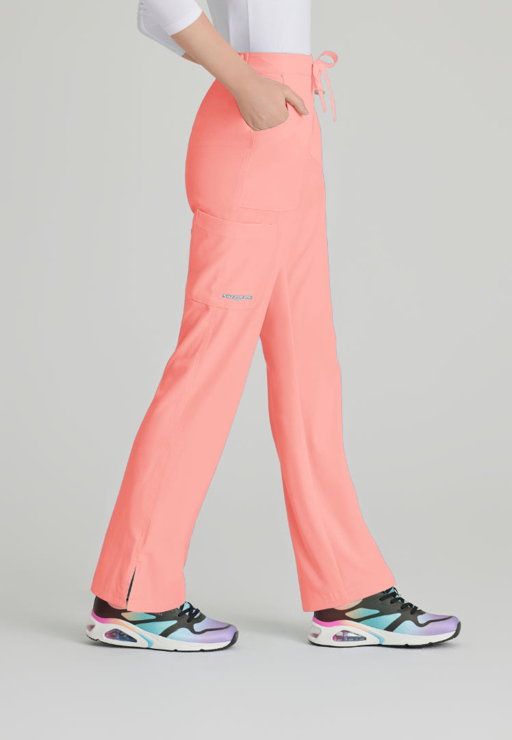 Side view of a woman wearing Skechers SK201 scrub pants in Coral Fizz and colorful sneakers on a light gray background