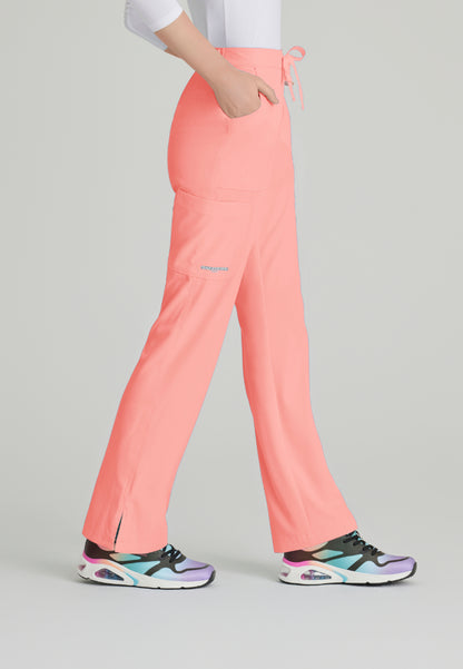 Side view of a woman wearing Skechers SK201 scrub pants in Coral Fizz and colorful sneakers on a light gray background