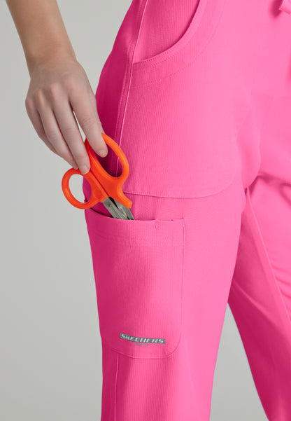 Detailed pocket view of a woman wearing Skechers SK201 Passion Pink scrub pants with a pocket holding orange scissors on a plain background