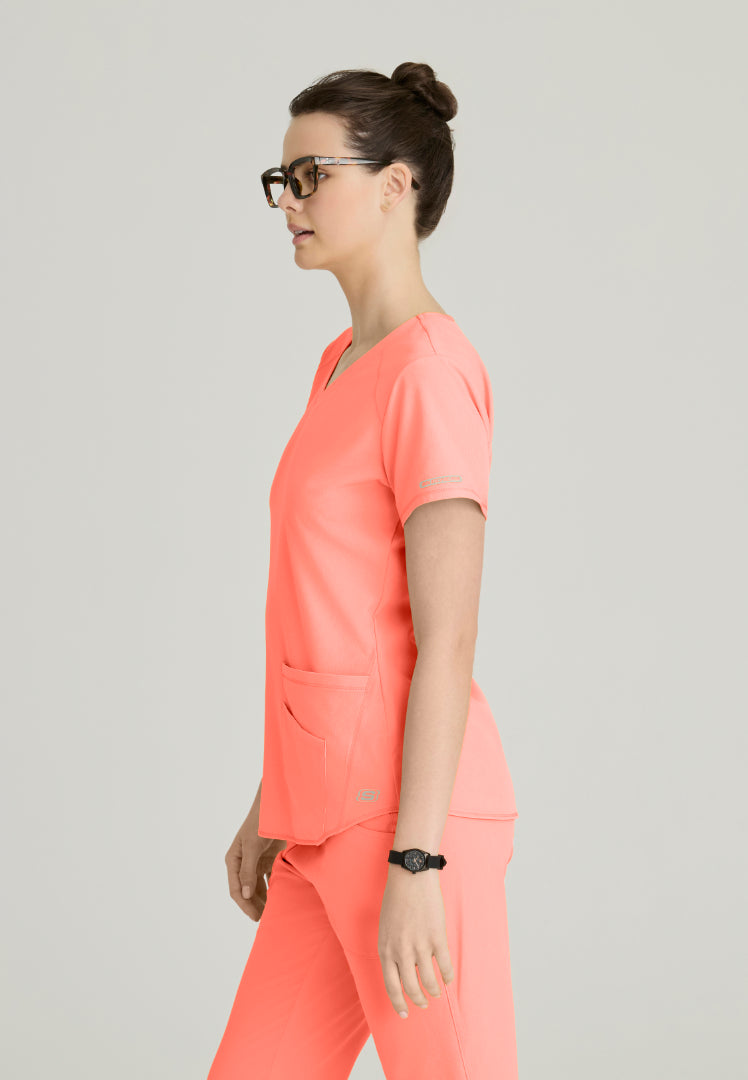 Side view of a woman wearing a Skechers Coral Fizz scrub set (SK101 top and SK201 pant) on a plain background