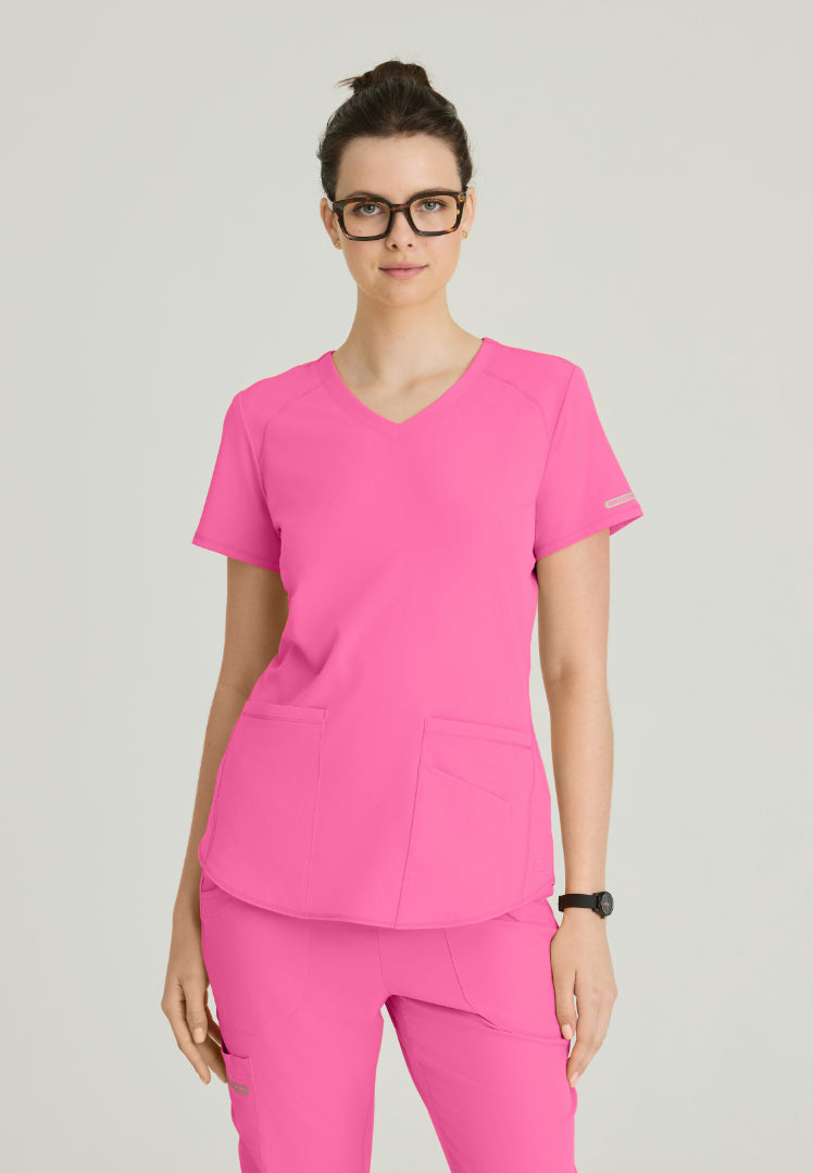 Woman wearing a Skechers SK101 Passion Pink scrub shirt on a gray background