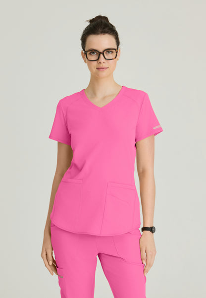 Woman wearing a Skechers SK101 Passion Pink scrub shirt on a gray background