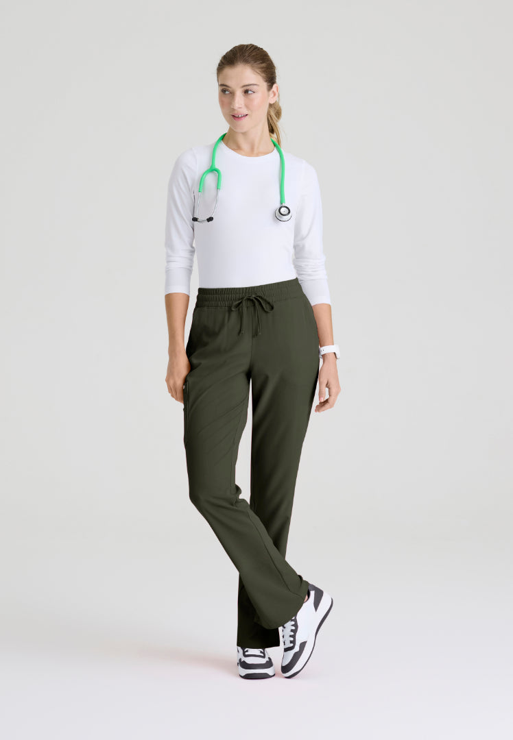 Front view of woman wearing a white underscrub shirt, olive green pants, and black sneakers on a light gray background