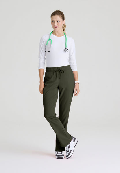 Front view of woman wearing a white underscrub shirt, olive green pants, and black sneakers on a light gray background