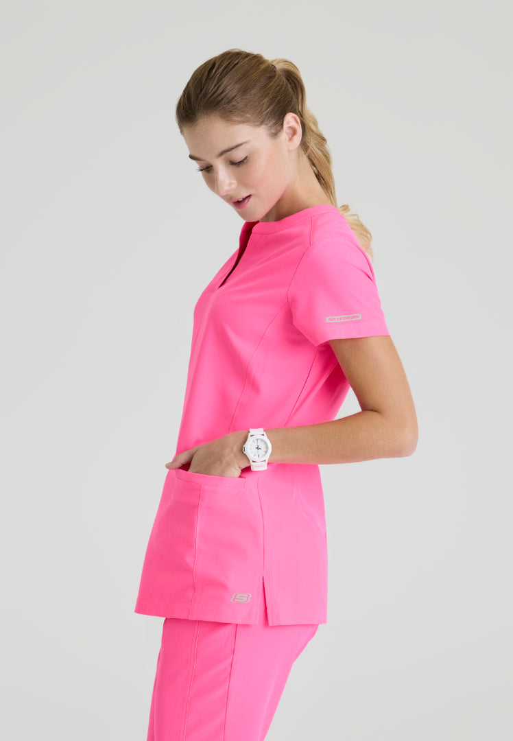 Side view of a woman wearing a Skechers SKT259 Passion Pink scrub shirt on a light gray background