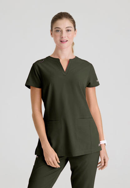 Woman wearing a Skechers SKT259 olive green scrub shirt on a light gray background