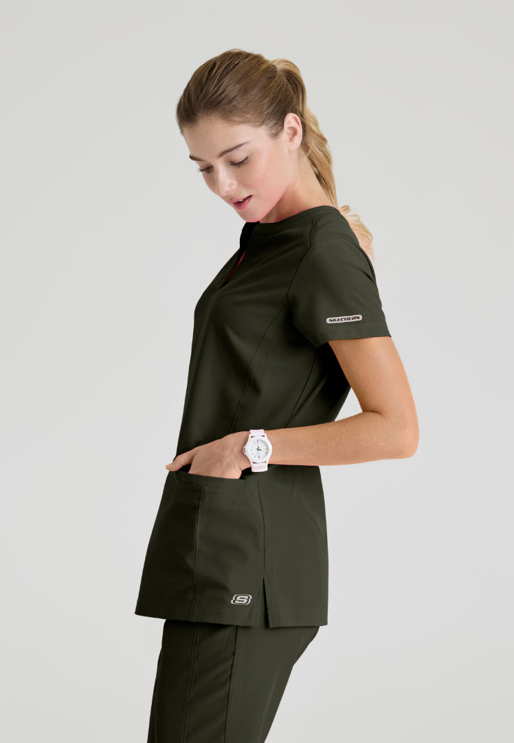 Side view of a woman wearing a Skechers SKT259 olive green scrub shirt on a light gray background