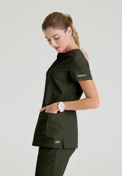 Side view of a woman wearing a Skechers SKT259 olive green scrub shirt on a light gray background