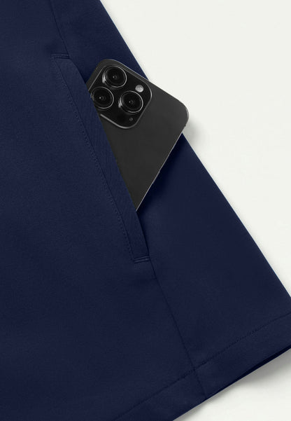 Detiled view showing a Jaanuu navy blue scrub top with a black smartphone peeking out of it's pocket on a white background