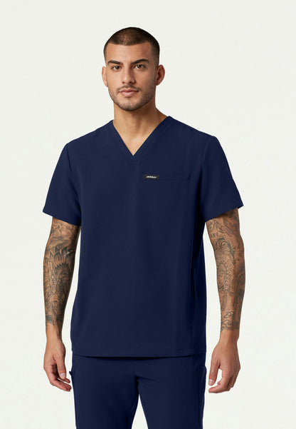 Man wearing a navy blue Jaanuu Platt v-neck scrub shirt on a light gray background
